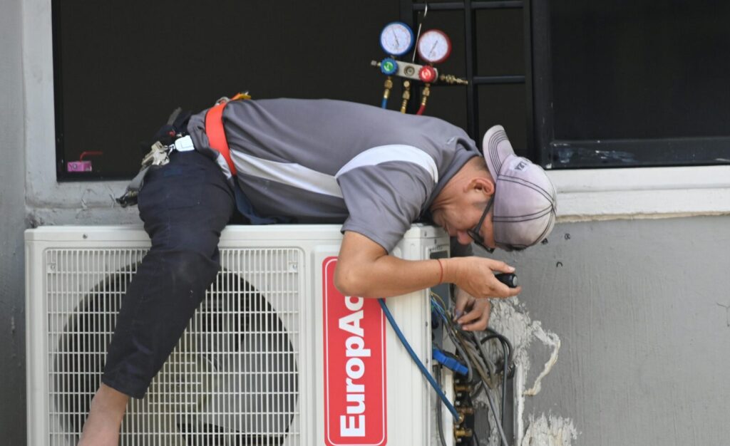 A technician skillfully repairing an outdoor air conditioning unit mounted on a building wall.